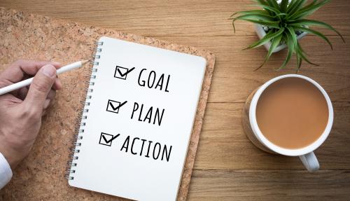 Checklist sitting on a desk with a hot drink and plant. Checklist has ticked goal, plan and action.