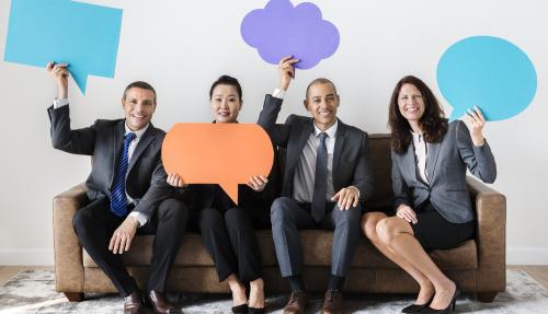 Four colleagues sitting on a couch in corporate attire holding up cardboard speech bubbles